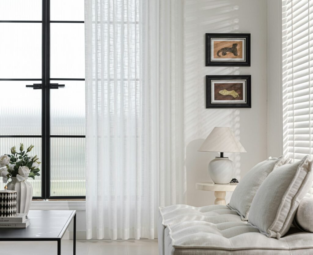 Salón luminoso y ordenado con cortinas blancas, sofá claro y lámpara de mesa