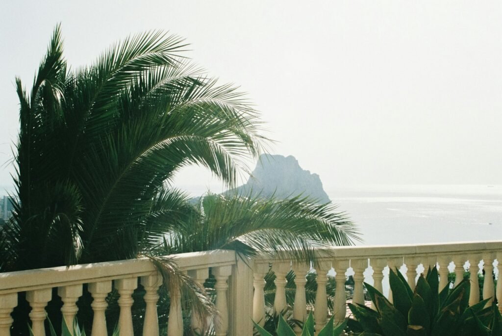 Balcón con balaustrada y palmeras frente al mar, con el Peñón de Ifach al fondo